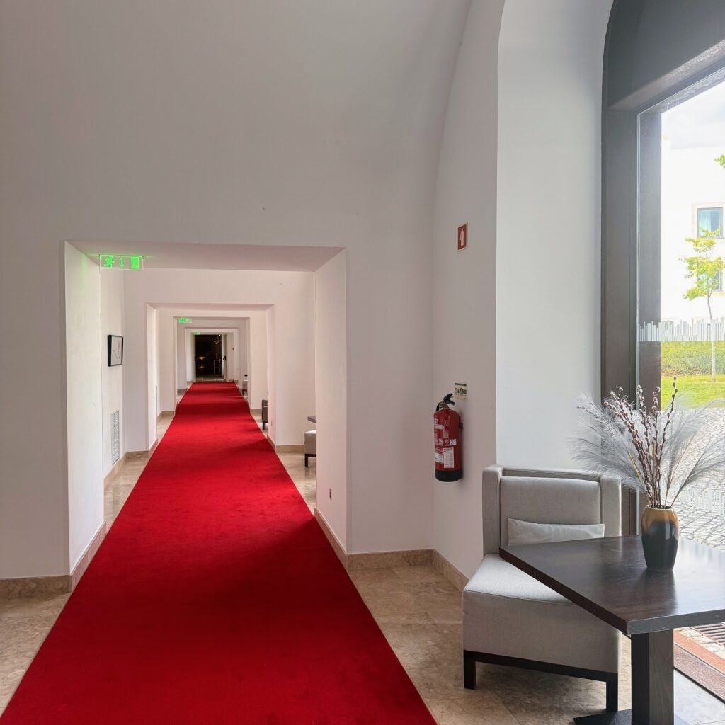 A red carpet running down a minimalist hallway in a Portugal small hotel, with natural light streaming in and cozy details by the door.