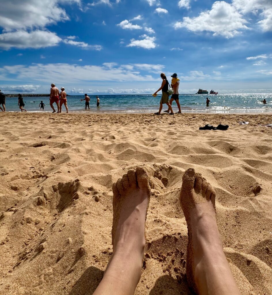 Feet in golden sand at Las Teresitas, Tenerife — couples beach day facing the Atlantic under blue skies.