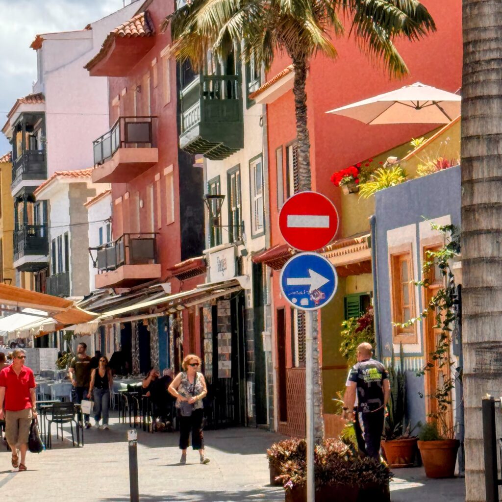 Colorful pedestrian street with cafés in Puerto de la Cruz old town — pastel façades, outdoor dining, Tenerife honeymoon mood.