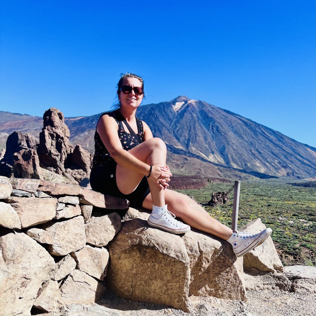 Woman sitting on volcanic rocks with Mount Teide behind — sunny day in Teide National Park, Tenerife.